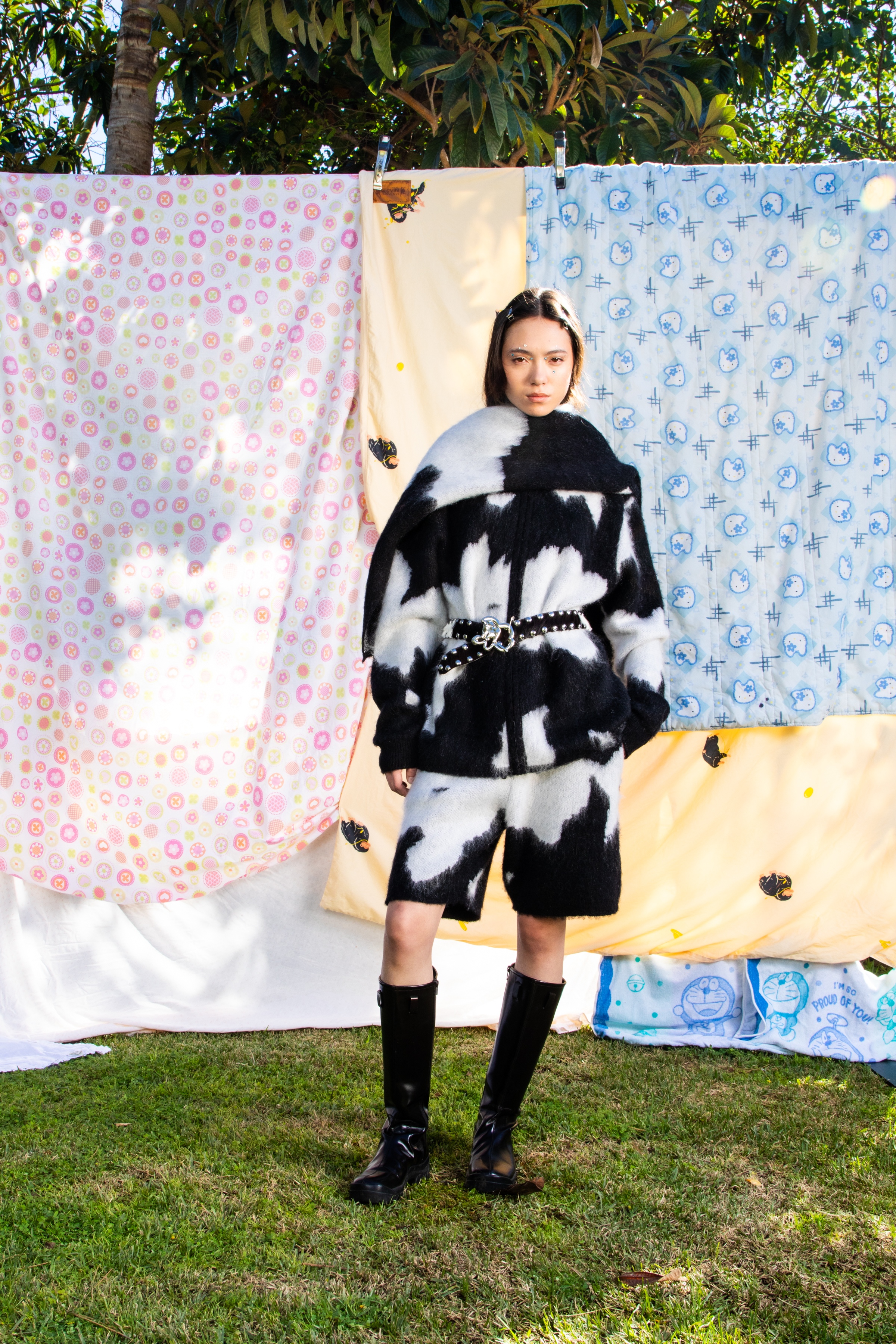 Full body image of a female model wearing matching cow print outift against a backdrop of patterned quilts.